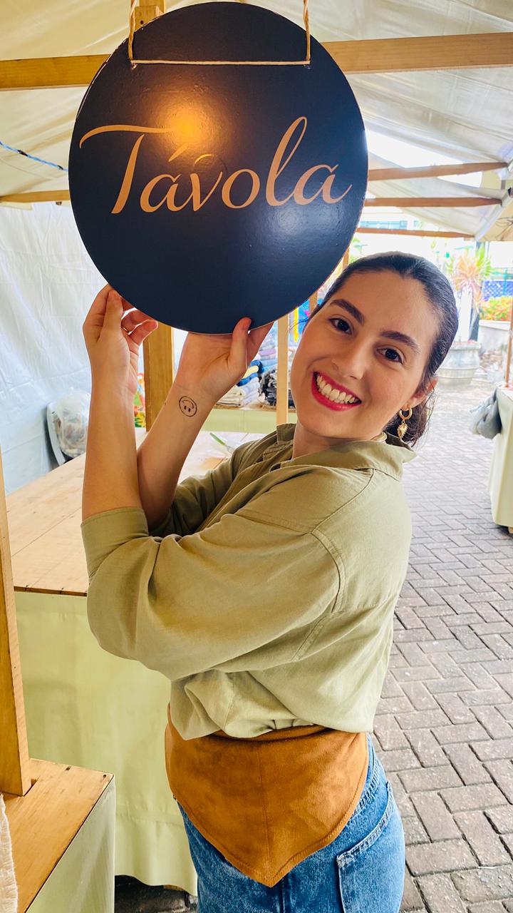 Gabriella Tanico sorrindo enquanto segura a placa da Tavola.